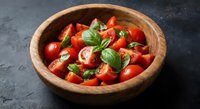 Fresh cherry tomato salad with basil leaves and mozzarella in wooden bowl on dark slate background for healthy Mediterranean cuisine and cooking.