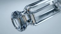 Clear glass laboratory vial with cylindrical neck and round opening against neutral background, used in scientific research and medical testing.