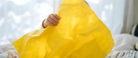 Young woman holding bright yellow bubble wrap packaging material in bedroom for stress relief and sensory therapy.