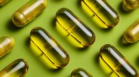 Transparent yellow omega-3 fish oil capsules arranged in rows on green background for health supplement and nutrition concept.