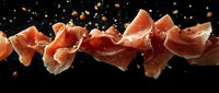 Slices of cured prosciutto ham arranged in a dynamic motion against black background, ideal for food photography, culinary design, restaurant menus, and gourmet food packaging.