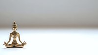 Golden Buddha statue in meditation pose on white background with copy space for mindfulness and spiritual wellness concepts.