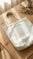 Blank white canvas tote bag on wooden table with dried eucalyptus, ceramic mug and natural sunlight, ready for branding, merchandise design and promotional use.