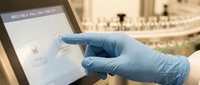 Medical professional in blue latex gloves using digital tablet interface in modern laboratory setting for healthcare technology and research applications.