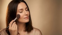 Young woman applying blush with makeup brush during beauty routine. Professional cosmetics application for natural glowing skin and daily skincare regimen.
