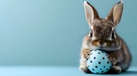 Adorable brown bunny holding light blue polka dot Easter egg against turquoise background. Festive spring holiday concept with copy space.