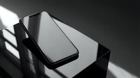 Modern black smartphone with blank screen lying on reflective dark surface with dramatic shadow patterns from window light creating minimalist tech composition.