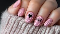 Pink polka dot nail art with heart and love text design on manicured nails against cozy knit sweater background, showcasing romantic Valentine's day style nail art.