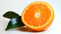 Fresh juicy orange cut in half showing bright pulp texture and green leaves, closeup view on light background for healthy eating and vitamin C concepts.