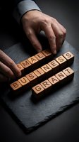 Businessman hands arranging wooden letter blocks spelling small business grant on dark slate surface for funding and entrepreneurship concepts.