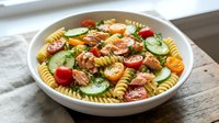 Fresh pasta salad with rotini, cherry tomatoes, cucumbers, and herbs in white bowl on wooden table for summer dining and meal prep.