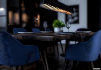 Modern restaurant interior with navy blue velvet chairs, dark wooden table, and contemporary black pendant lamp creating moody atmospheric lighting.