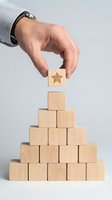 Male hand placing wooden block with star symbol on top of pyramid stack, representing success, achievement, and business growth strategy.