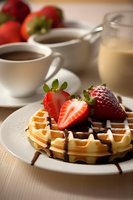 Fresh Belgian waffle topped with sliced strawberries and chocolate sauce, served with coffee and cream for breakfast. Selective focus on waffle plate.