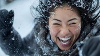 Young Asian woman laughing joyfully with flying hair in winter snow, expressing genuine happiness and carefree emotion during snowfall, natural lifestyle portrait.
