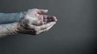 Elderly hands cupped together in protective gesture showing care, support and compassion against dark background for healthcare concepts.