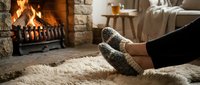 Woman relaxing by fireplace wearing cozy knitted socks on soft rug in warm living room interior for comfort and hygiene lifestyle concepts.