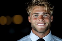 Young Caucasian businessman with blonde hair and beard wearing white shirt and tie smiles confidently against dark background with bokeh lights. Professional portrait.