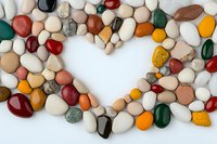 Colorful polished stones and pebbles arranged in heart shape on white background, natural mineral collection displaying variety of colors and textures.