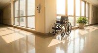 Empty wheelchair in modern hospital corridor with large windows and natural sunlight streaming across polished floors for healthcare accessibility concepts.