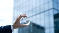 Professional businessman holding crystal sphere with city reflection against modern glass office building background for business vision concepts.