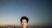 Young woman with short dark curly hair and warm smile against twilight sky backdrop. Outdoor portrait for lifestyle, beauty, and professional use.
