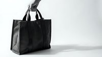 Black leather tote bag held by hand against white background, minimalist fashion accessory for shopping and everyday use isolated on white.