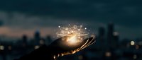Silhouetted hand holding glowing light bulb with digital network icons above city skyline at dusk, representing innovation, ideas, and technology solutions for business and creative projects.