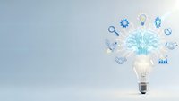 Light bulb with glowing brain and business icons floating above representing innovation, creativity and entrepreneurial thinking for corporate success.
