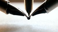 Two fountain pen nibs meeting at a point on white paper, creating a symmetrical composition for writing, calligraphy, and stationery design projects.