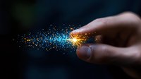 Magical glowing sparkles trail from human finger against dark background, creating ethereal light effect with blue and golden particles streaming in space.