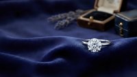 Elegant diamond engagement ring on luxurious navy blue silk fabric with vintage jewelry box and lavender sprigs creating romantic wedding proposal scene.