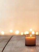 Glowing candle in glass jar on wooden surface with soft bokeh lights in background creates peaceful atmosphere for wellness and meditation spaces.