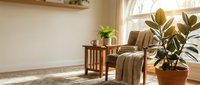 Cozy reading corner with wooden chair, soft throw blanket and potted plants in sunlit room with natural light streaming through arched window.