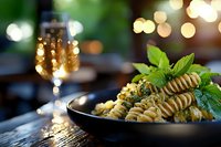 Fusilli pasta with fresh basil and parmesan served on dark plate against blurred bokeh lights background, elegant restaurant atmosphere and wine glass.