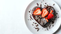 Heart shaped chocolate cake topped with fresh strawberry slices and chocolate shavings on white plate against light background, romantic dessert.
