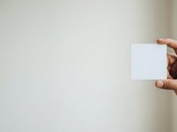 Hand holding blank white card against neutral beige wall background. Isolated mockup for business branding, corporate identity, greeting card design, and marketing materials presentation.