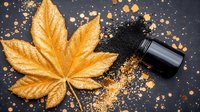 Golden metallic cannabis leaf with black essential oil bottle and scattered glitter on dark background, creating luxurious spa and wellness composition.