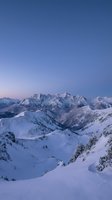 Aerial view of snow-covered alpine peaks and frozen mountain lakes at dawn, with clear blue sky. Suitable for travel, nature, and winter landscape projects.