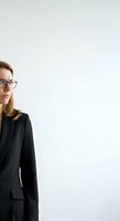 Professional woman with shoulder-length blonde hair and glasses wearing black blazer against white background, suitable for corporate, business, and professional portraits.