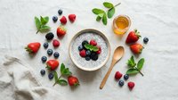 Fresh berries and chia seed pudding arranged on white marble surface with mint leaves and honey for healthy breakfast or dessert styling.