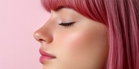 Young Asian woman with pink hair and closed eyes in profile view against soft pink background, showcasing natural makeup and serene expression.