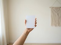 Hand holding blank white card in minimalist interior space with natural light, suitable for mockup, branding, and advertising purposes.