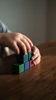 Child hands stacking colorful wooden building blocks on a wooden table, showcasing early learning, creativity, and motor skill development.