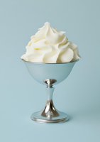 Creamy whipped topping served in vintage coupe glass with metallic stem on soft blue background, ready for dessert and food styling projects.