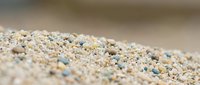 Close-up of sand grains with small blue pebbles and shells scattered throughout, suitable for beach, nature, and travel-related projects.