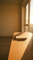 Minimalist wooden desk with open notebook in sunlit room, warm golden light streaming through window, empty workspace for creative work and productivity concepts.