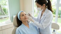 Professional dermatologist performing facial injection treatment on relaxed female patient in modern medical clinic setting.