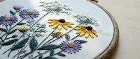 Hand embroidered wildflower bouquet with purple asters and yellow black-eyed susans in wooden hoop on natural linen fabric for needlework crafts.