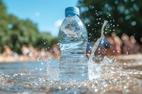 Clear plastic water bottle with splashing water droplets against blurred summer beach background, dynamic motion capture in bright sunlight.